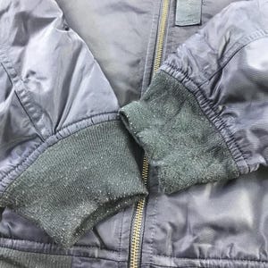 Puede incluir: Una chaqueta bomber azul oscuro con cierre de cremallera y pu&ntilde;os de punto de canal&eacute;. La chaqueta tiene un aspecto ligeramente desgastado.