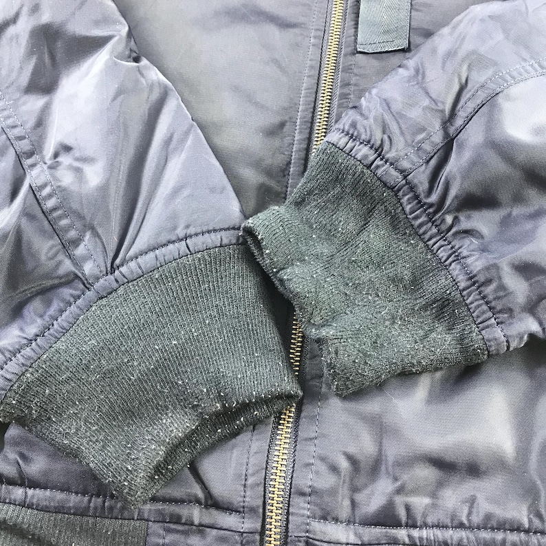 Puede incluir: Una chaqueta bomber azul oscuro con cierre de cremallera y pu&ntilde;os de punto de canal&eacute;. La chaqueta tiene un aspecto ligeramente desgastado.