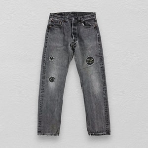 May include: Black denim jeans with multiple circular patches. The patches are made of a black fabric with white stitching.