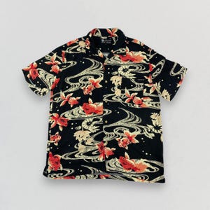 May include: Black short-sleeve button-up shirt with a vibrant pattern of red and orange koi fish, cream-colored flowers, and swirling water designs. The shirt has a classic collar and a relaxed fit, perfect for casual wear.