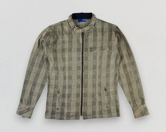 May include: A tan and gray checkered jacket with a black zipper closure. The jacket has a stand-up collar, two side pockets, and a small chest pocket. The long-sleeved jacket is made of a textured material.