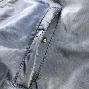 Puede incluir: Primer plano de una chaqueta azul oscuro con cremallera y un bolsillo en el lado izquierdo. El bolsillo tiene un cierre de bot&oacute;n.