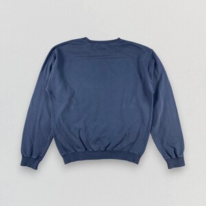 May include: A solid navy blue crew neck sweatshirt. The long-sleeved top has a relaxed fit with ribbed cuffs and hem. The garment is made of a soft, comfortable material, perfect for casual wear.