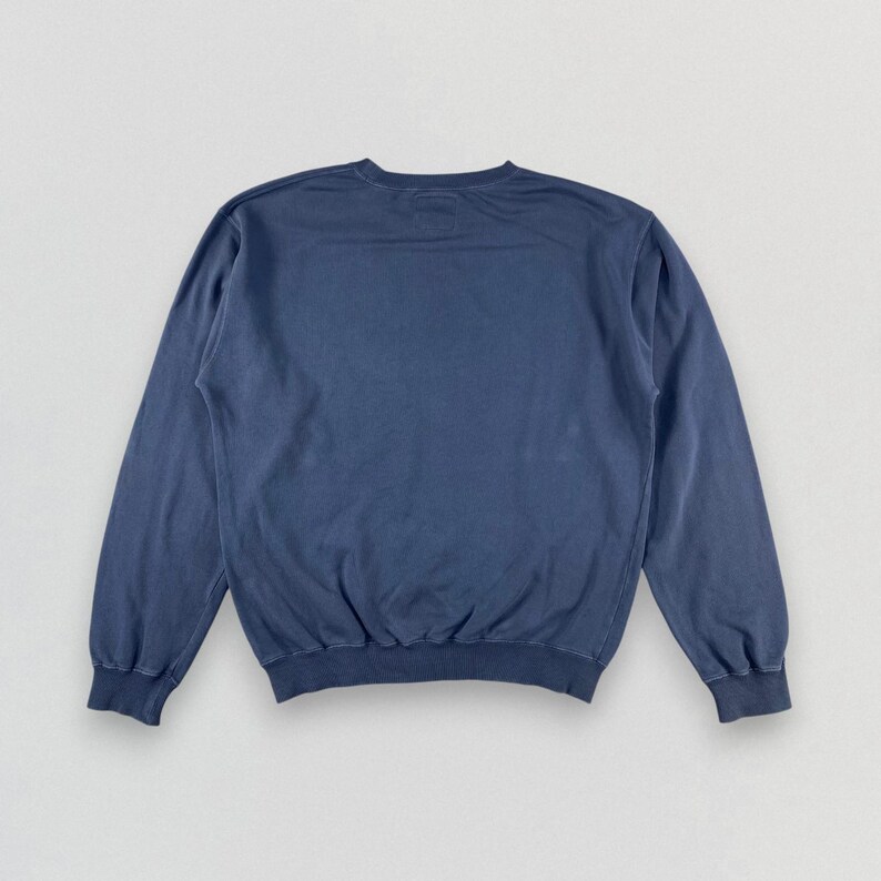 May include: A solid navy blue crew neck sweatshirt. The long-sleeved top has a relaxed fit with ribbed cuffs and hem. The garment is made of a soft, comfortable material, perfect for casual wear.