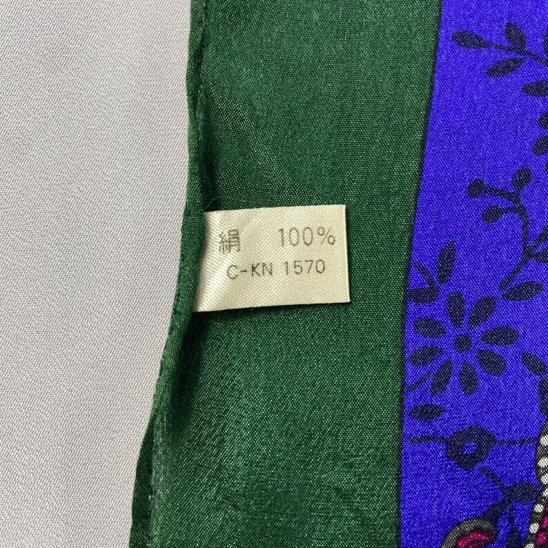 May include: A green and blue silk scarf with a floral pattern. The tag on the scarf reads "絹 100% C-KN 1570".