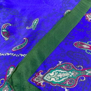 May include: A blue and green paisley patterned silk scarf with a dark green border. The scarf is folded in half, with the patterned side facing out.