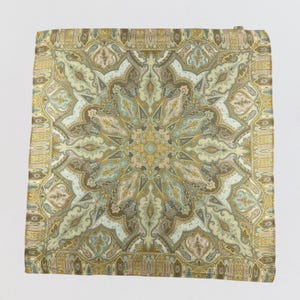 May include: Square silk scarf with a detailed paisley pattern in shades of beige, brown, gold, and pale blue. The design features a central floral motif surrounded by intricate, repeating elements. The scarf has a delicate, ornate border.