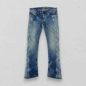Könnte beinhalten: Blaue Jeans aus Denim mit heller Waschung und einem markanten weißen Schlangenledermuster entlang der äußeren Beinnähte. Die Jeans verfügt über einen klassischen Knopfverschluss, Vordertaschen und eine Fünf-Taschen-Konstruktion.