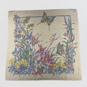 May include: A square silk scarf in a light beige tone featuring a printed border of blue lines. The design displays a variety of colorful flowers in shades of pink, yellow, and blue, accompanied by two butterflies in flight. The signature is visible.