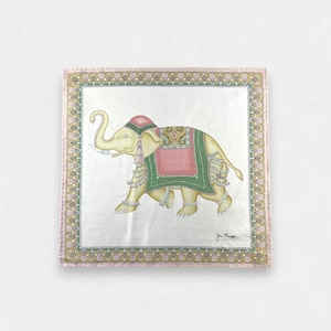 May include: A square silk scarf featuring a central illustration of a cream-colored elephant adorned with a pink and green decorative blanket, headpiece, and tassels. The scarf has a wide, ornate border in shades of gold, pink, and green.