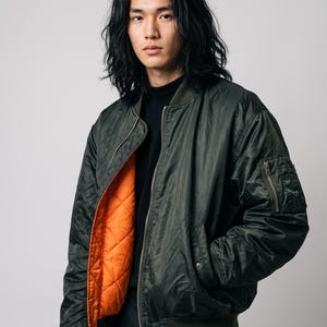 Puede incluir: Una chaqueta bomber de color verde oliva con cremallera frontal plateada, cuello y puños acanalados, y un forro acolchado de color naranja brillante. La chaqueta incluye un bolsillo utilitario con cremallera en la manga izquierda y dos bolsillos laterales.
