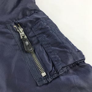 Puede incluir: Una chaqueta bomber azul marino con cierre de cremallera y un bolsillo con solapa en el lado izquierdo. El bolsillo tiene cierre de cremallera y se asegura con un bot&oacute;n a presi&oacute;n.