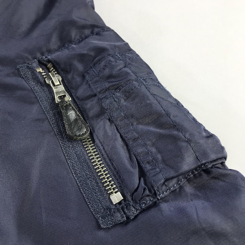 Puede incluir: Una chaqueta bomber azul marino con cierre de cremallera y un bolsillo con solapa en el lado izquierdo. El bolsillo tiene cierre de cremallera y se asegura con un bot&oacute;n a presi&oacute;n.