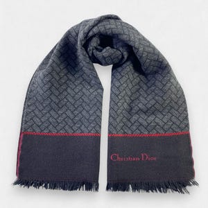 May include: A black and gray patterned scarf with a red embroidered border and the text "Christian Dior" in red. The scarf has a fringed edge.