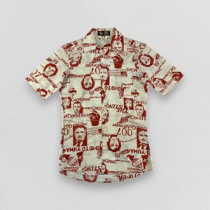 May include: Short-sleeved button-up shirt with a cream-colored background and a repeating pattern of red-toned movie-themed graphics, including portraits and text. The shirt has a classic collar and button closure.