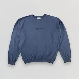 May include: A faded blue Gramicci sweatshirt with a crew neck and long sleeves. The brand name is printed in black script across the chest. The sweatshirt has a relaxed fit and a vintage aesthetic.