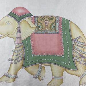 May include: A printed textile featuring a stylized elephant in shades of cream, pink, and green. The elephant wears a decorative headpiece, a large saddle blanket with floral patterns, and multiple strands of hanging bells and beaded jewelry.