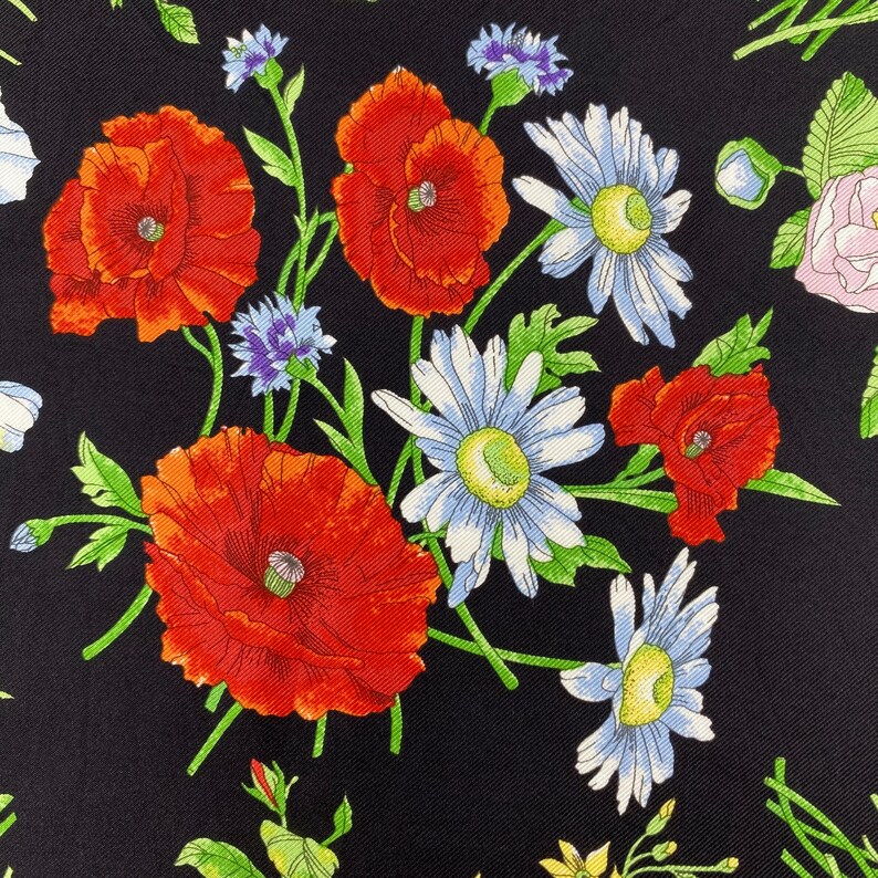Puede incluir: Tela negra con un estampado floral. El patr&oacute;n incluye amapolas rojas, margaritas blancas y acianos azules, con hojas y tallos verdes. Primer plano de un patr&oacute;n floral repetido.