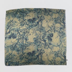 May include: A square scarf featuring a repeating pattern of dark blue skulls intertwined with detailed floral vines against a light beige background. The fabric displays a consistent print of botanical elements and skeletal motifs throughout.