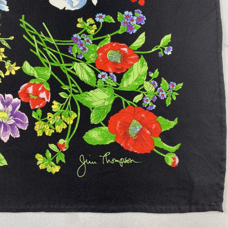 Puede incluir: Pa&ntilde;uelo cuadrado negro con un dise&ntilde;o floral. El dise&ntilde;o incluye amapolas rojas, flores moradas y azules y hojas verdes. La firma Jim Thompson es visible.