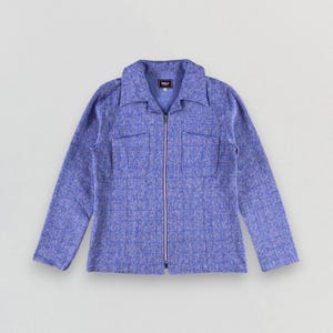May include: A periwinkle blue jacket with a textured, grid-like pattern. The jacket features a collared neckline, a full-length silver zipper, and two square chest pockets. The long sleeves and tailored fit suggest a vintage or retro style.