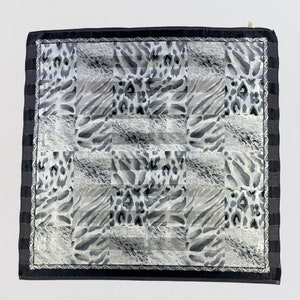 May include: Square silk scarf with a black border and a repeating pattern of animal print squares in shades of gray and white. The scarf has a striped border with gold accents.