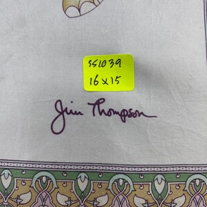 May include: A light-colored fabric featuring a decorative border with green, gold, and pink patterns. A yellow sticker displays the text 551039 and 16x15 inches. The signature Jim Thompson is printed in dark purple script below the sticker.