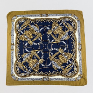 Op de afbeelding: Een vierkante zijden sjaal met een diep marineblauw middenstuk met een symmetrisch patroon van goud- en zilverkleurige ruiteraccessoires, zoals stijgbeugels en gespen, omringd door een crèmekleurige rand en een brede, effen mosterdgele buitenrand.