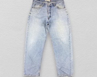 May include: Light blue denim jeans with a relaxed fit. The jeans have a button fly and five pockets. The waistband has a brown leather patch with the text "CLASSIC FIT" printed on it.
