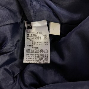 Puede incluir: Una etiqueta de ropa azul marino con texto blanco y s&iacute;mbolos. La etiqueta incluye el texto "GU", "311-277515(64-01)" y una lista de materiales e instrucciones de cuidado.