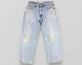 May include: Light blue denim jeans with faded spots and a small tear on the left leg. The jeans have a button fly and five pockets.