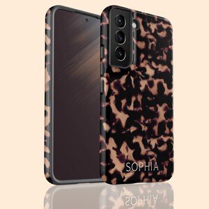 Op de afbeelding: Een zwarte telefoonhoes met een schildpadpatroon en de naam "Sophia" gedrukt op de achterkant.