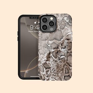 Könnte beinhalten: Eine Smartphone-Hülle mit einem detaillierten Schlangenledermuster in Beige-, Braun- und Schwarztönen. Die Hülle verfügt über einen Ausschnitt für das Kameraobjektiv und zeigt die Buchstaben YK in einer dezenten Schrift unten in der Mitte.