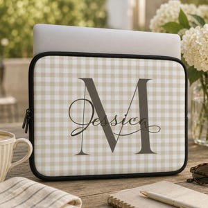 Puede incluir: Una funda rectangular para portátil con un patrón de cuadros vichy en beige y blanco. En el centro, una letra M mayúscula grande en gris oscuro con el nombre Jessica escrito en una fuente cursiva superpuesta sobre la letra en gris oscuro.