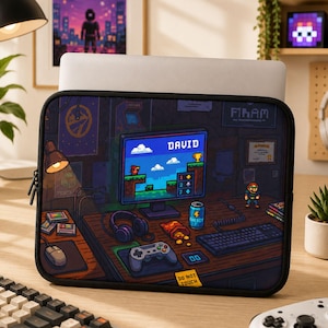 May include: A rectangular laptop sleeve featuring a pixel art illustration of a gaming desk. The screen displays the name DAVID, a score board, and a platform game. Accessories include a controller, headphones, a mouse, and an energy drink.