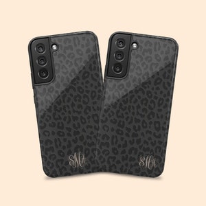 May include: Two black phone cases with a leopard print design and a monogrammed initial "SMA" in a light gold color.