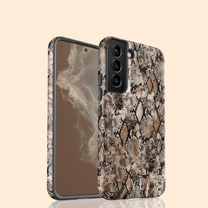 May include: A smartphone case featuring a brown, black, and beige snakeskin pattern. The case covers the back and sides of the phone, with a cutout for the triple camera lens array. The design includes a subtle monogram at the bottom center.