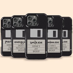 Peut inclure: Une collection de cinq coques de smartphone noires conçues pour ressembler à des disquettes vintage. Chaque coque présente une étiquette gris clair avec du texte personnalisé, incluant des noms de fichiers comme smile.exe et des noms.