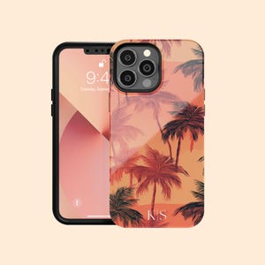 Könnte beinhalten: Eine transparente Handyhülle mit einem tropischen Palmenmuster in Orange-, Rot- und Grüntönen. Die Hülle trägt die Initialen "KS" in Weiß unten. Die Handyhülle ist auf einem schwarzen iPhone mit einem Bildschirm zu sehen, der die Zeit "9:41" und das Datum "Dienstag, September" anzeigt.