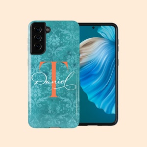 Puede incluir: Una funda para teléfono azul turquesa con un patrón de damasco y una gran letra naranja "T" con el nombre "Daniel" escrito en cursiva blanca.