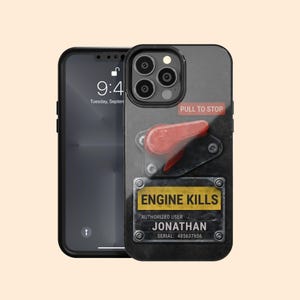 Op de afbeelding: Zwarte iPhone-hoes met een ontwerp dat lijkt op een motorbedieningspaneel. De hoes heeft een rode hendel met "PULL TO STOP" en een gele plaat met "ENGINE KILLS", de naam "JONATHAN" en een serienummer.
