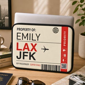 May include: A rectangular laptop sleeve featuring a cream-colored design that mimics an airline luggage tag. It displays the text PROPERTY OF: EMILY, LAX, JFK, and VIP PASSENGER - SUPER CHILL, along with a black airplane icon, a barcode, and a red stripe.