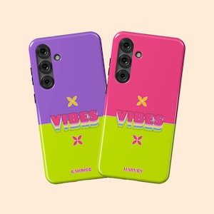 May include: Two phone cases with a split design. One is purple and green, the other pink and green. Each case has the word "VIBES" in colorful, layered text, along with a small flower graphic and a name at the bottom.