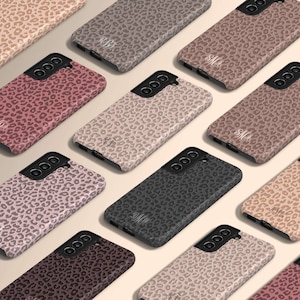 May include: Assortment of phone cases with a leopard print design in various colors. Each case has a monogrammed initial in white.