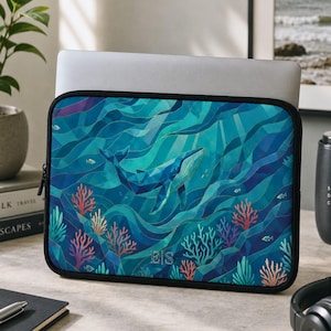 May include: A rectangular laptop sleeve featuring a geometric, stained-glass style illustration of a blue whale swimming through deep blue ocean waves, surrounded by colorful coral reefs and small fish, with the letters E|S printed at the bottom.