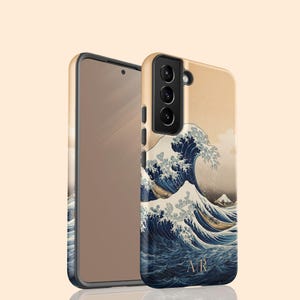 May include: Two phone cases with a design inspired by the famous Japanese artwork, "The Great Wave off Kanagawa." The cases feature a beige background with a large blue wave and a mountain in the distance. The initials "AR" are at the bottom.