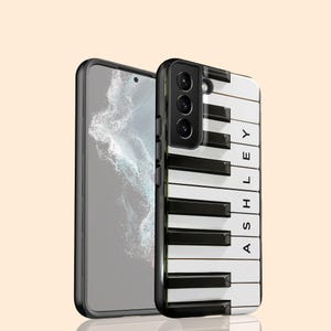 Könnte beinhalten: Eine schwarze Smartphone-Hülle mit einem Klaviertasten-Design mit schwarzen und weißen Tasten. Der Name "ASHLEY" ist vertikal auf der rechten Seite der Hülle aufgedruckt. Ein zweites Smartphone ist links zu sehen.