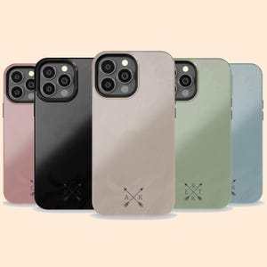 May include: Five different coloured phone cases with a minimalist design featuring a pair of crossed arrows and initials. The cases are rose gold, black, beige, green, and blue.