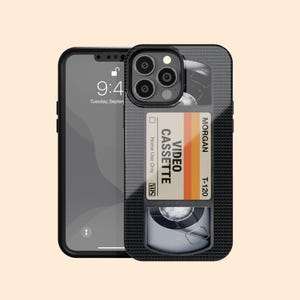 May include: Black iPhone case featuring a retro VHS tape design. The case has a black grid pattern and a label with the text "VIDEO CASSETTE" and "MORGAN T-120". The phone displays the time as 9:40 AM.