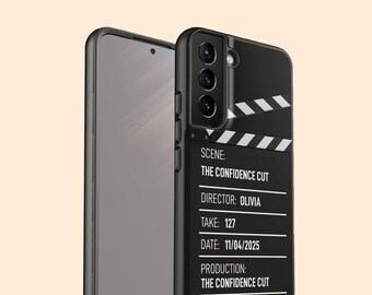 May include: A black smartphone case featuring a film clapperboard design with white text that reads SCENE: THE CONFIDENCE CUT, DIRECTOR: OLIVIA, TAKE: 127, DATE: 11/04/2025, and PRODUCTION: THE CONFIDENCE CUT, displayed alongside a smartphone with a dark screen.